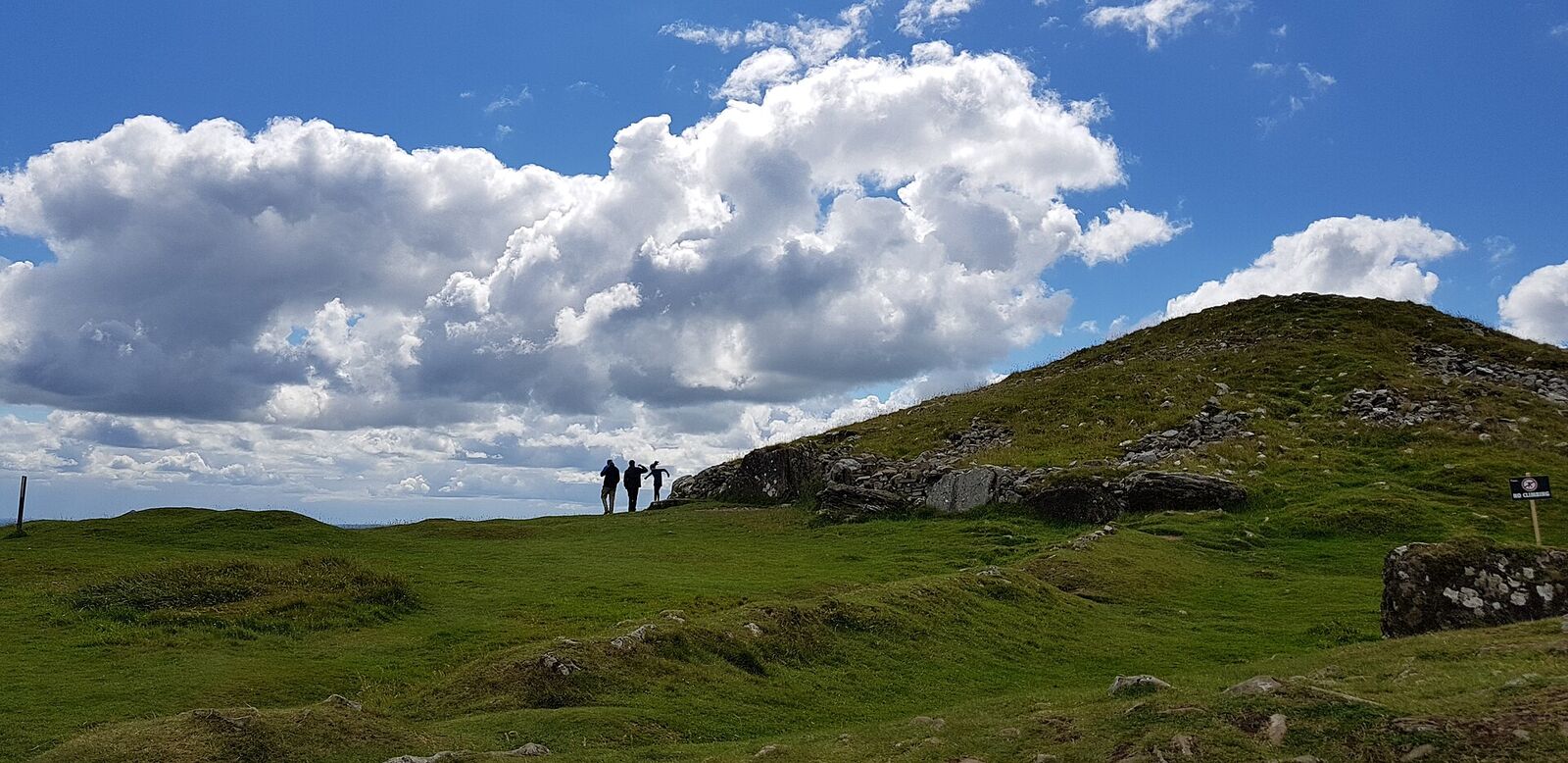 A grassy hilltop with a prehistoric stone cairn under a summer sky