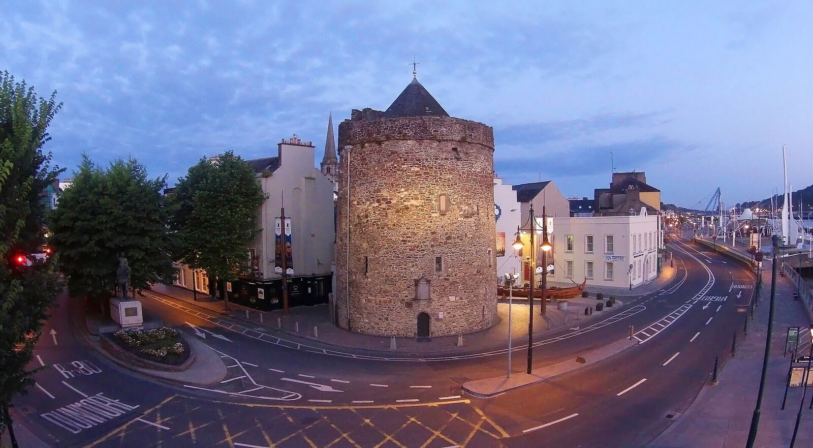 A round stone tower at the end of a city quay at dusk